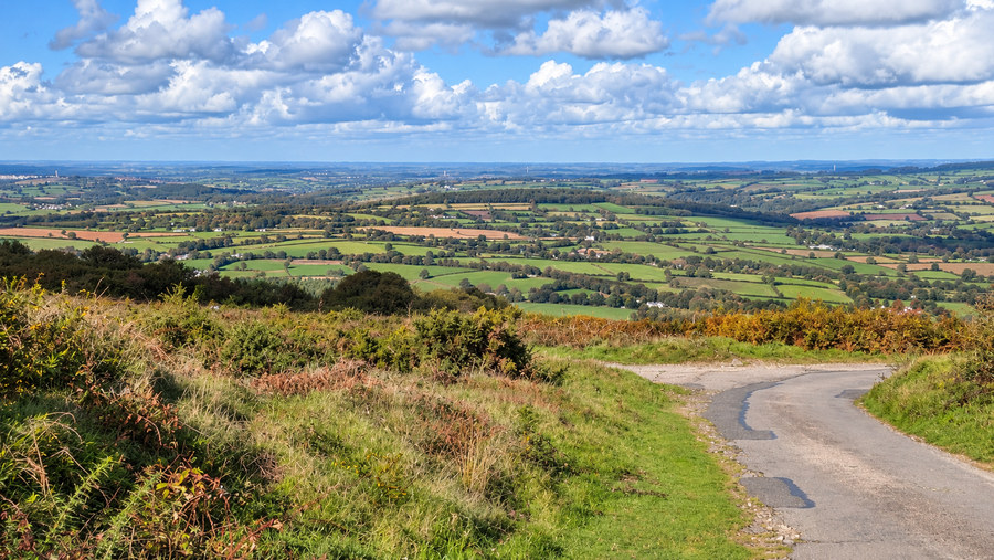 A narrow road curving downhill from Kit Hill, overlooking farmland