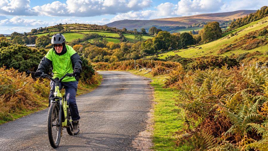 Dennis cycling on a narrow Dartmoor road amid hills and bracken